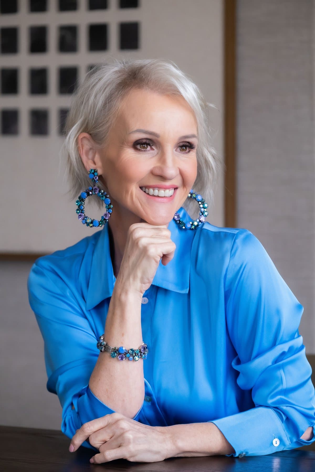 Linda in a blue satin blouse with blue statement earrings, smiling