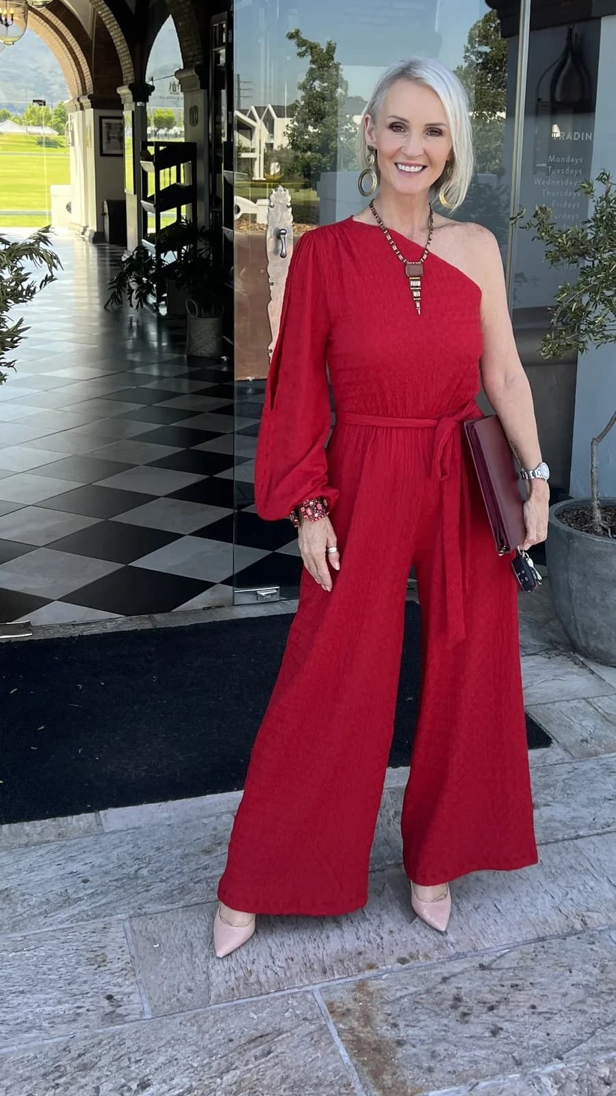 Linda in a red one-shoulder jumpsuit with nude heels and a clutch