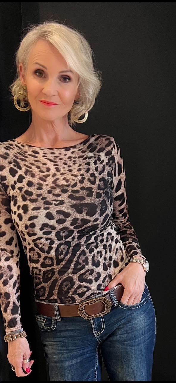 Linda Paige in a leopard print top with gold earrings, confident pose against dark background