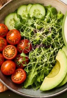 A bowl of salad with cherry tomatoes, cucumber, microgreens and sliced avocado.