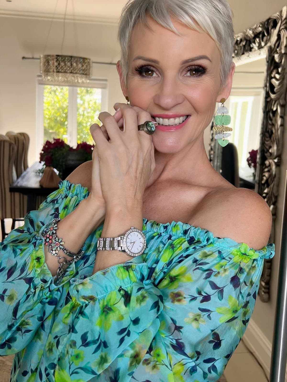 Linda in a turquoise floral off-the-shoulder top, hands clasped at her chin, smiling