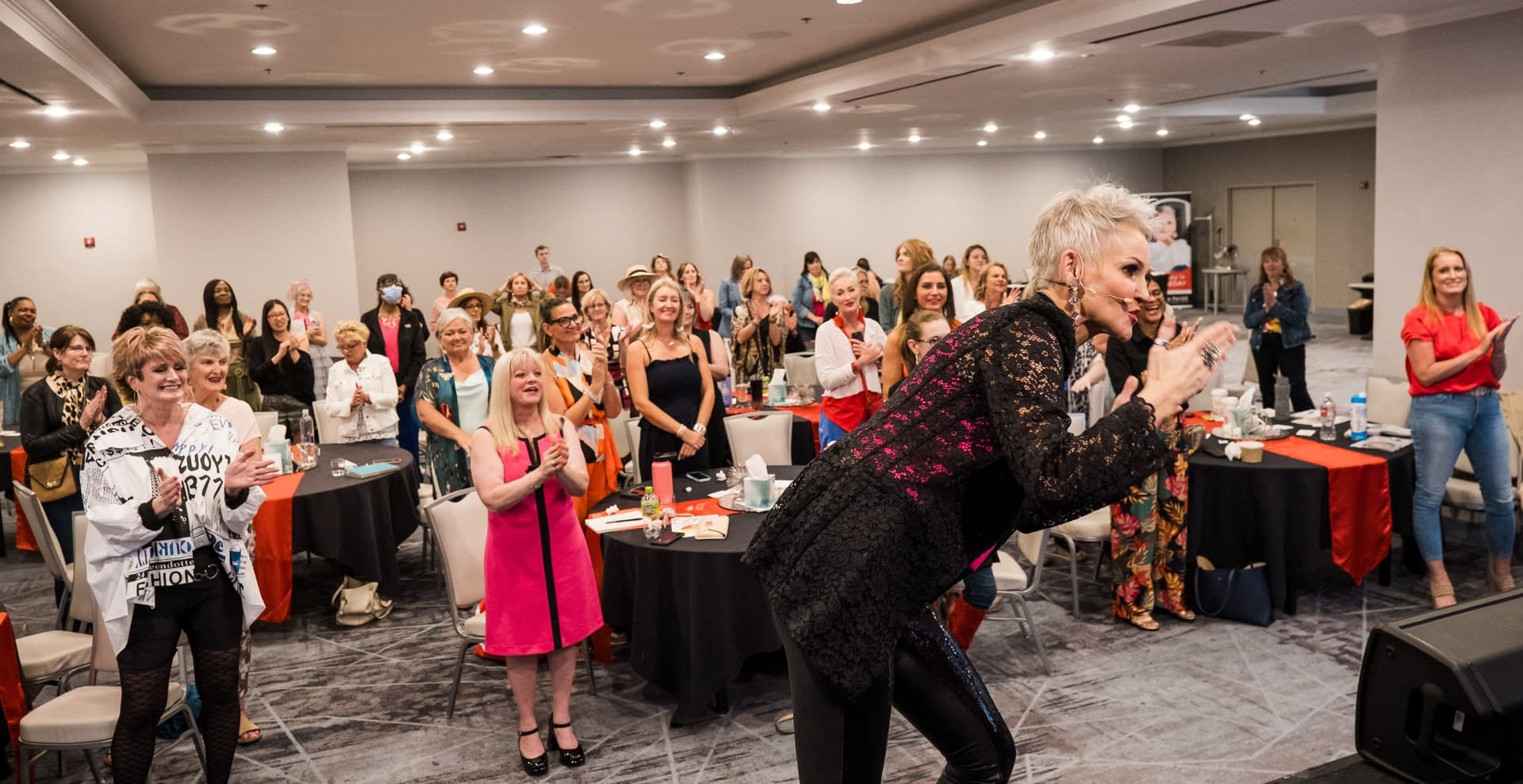 Linda Paige applauding on stage with the room on its feet at Linda Paige Live