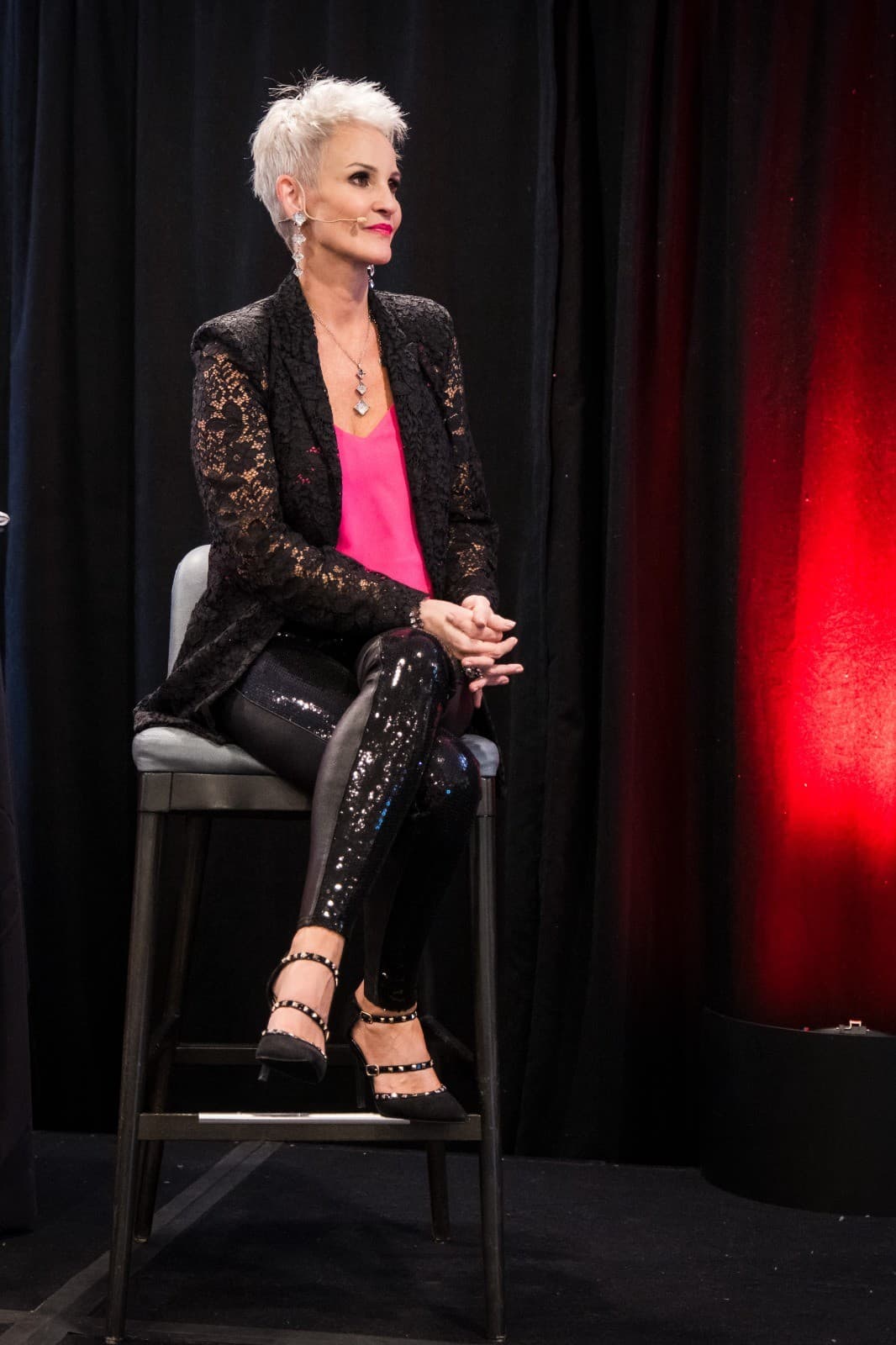 Linda Paige seated on a stool on stage in a black lace jacket