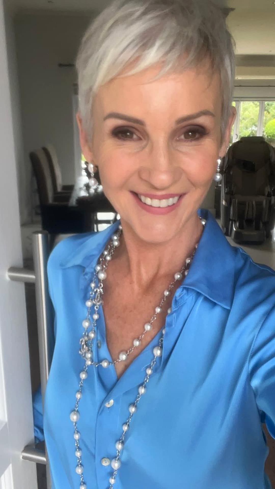 Linda in a blue shirt and a long string of pearls, smiling